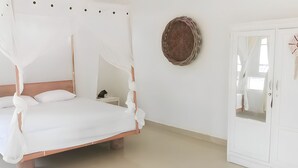A white four-poster bed with a wooden headboard, a bedside table with a lamp, and a wardrobe with a mirror. - THE VILLAGE INN Rua Beach  (Wanokaka)