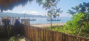 A wooden fence, a thatched roof, and a view of boats on a calm sea with distant mountains. - THE VILLAGE INN Rua Beach  (Wanokaka)