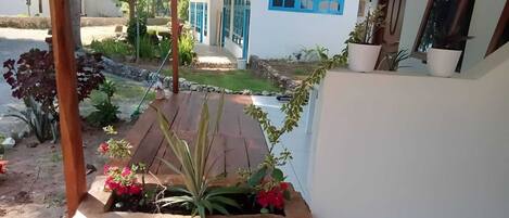 A wooden deck with potted plants and flowers, leading to a white building with blue doors and windows.