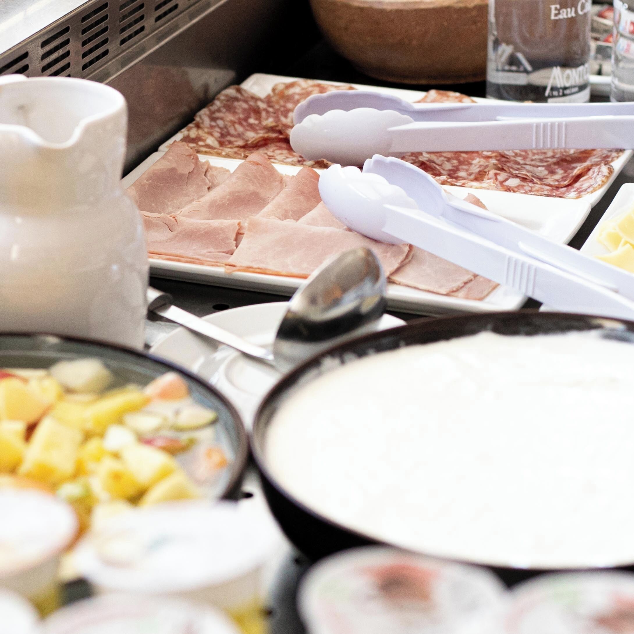 A buffet with various food items including sliced meats, a bowl of soup, and a pitcher.