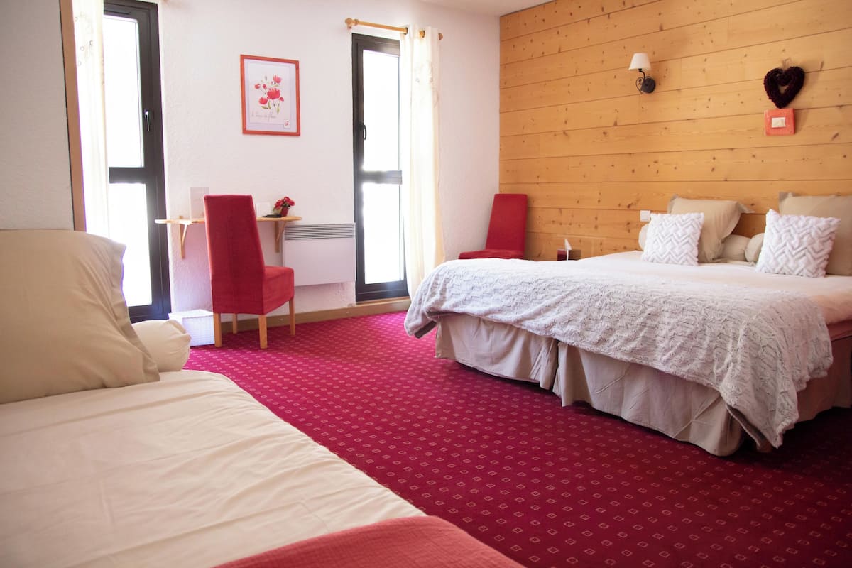 A hotel room with a red carpet, a bed with white bedding, a red chair, and a desk with a red chair.