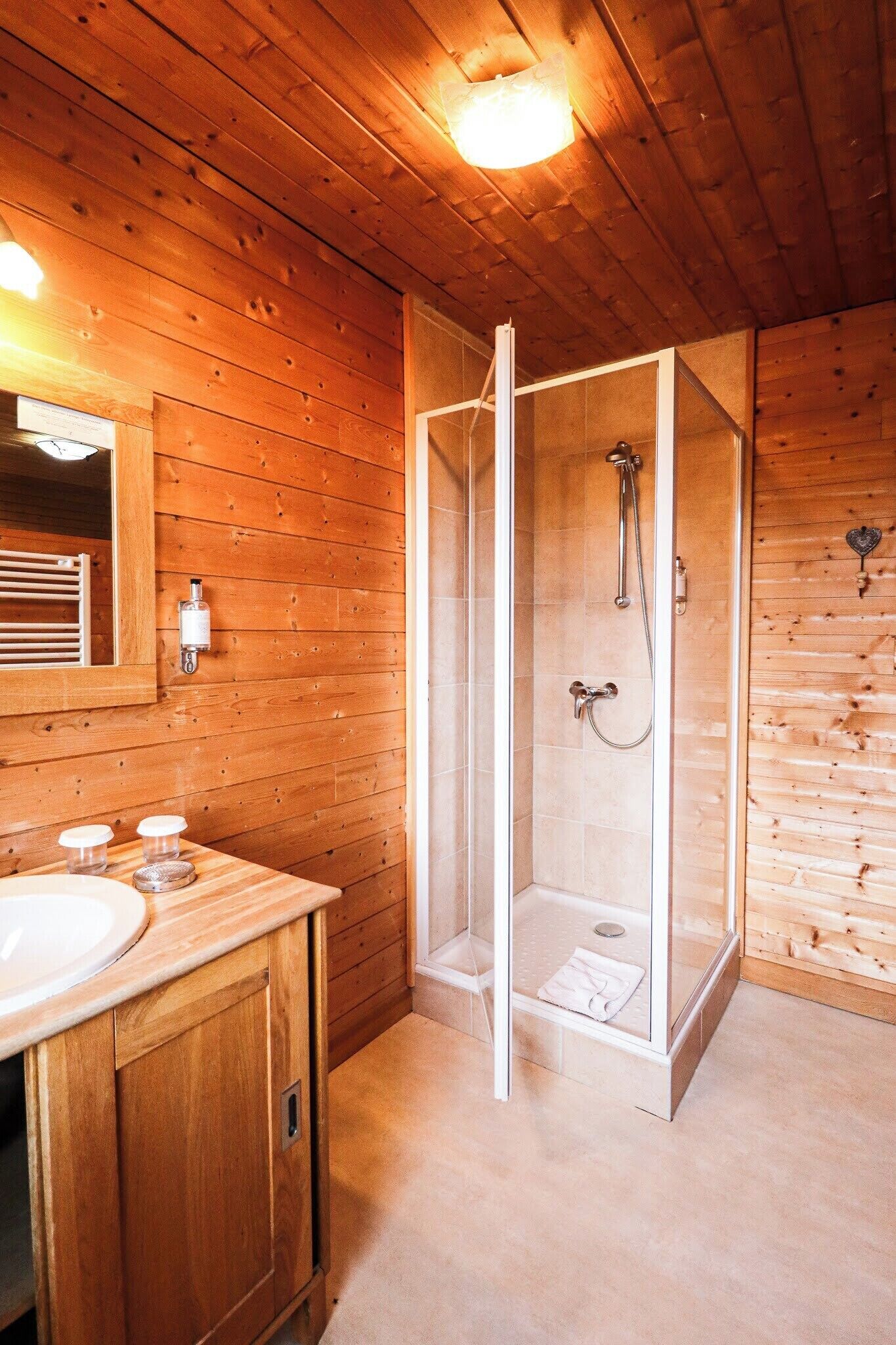A wooden cabin bathroom with a glass-enclosed shower, wooden cabinets, and a large mirror.