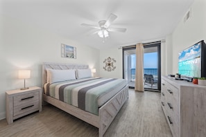 A bedroom with a bed, bedside tables, a ceiling fan, a TV, and a view of the outdoors.