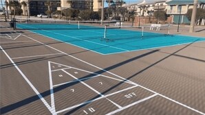 A shuffleboard court with numbered scoring areas and a pool table in the background. - Wind Drift South East 404 (Orange Beach)