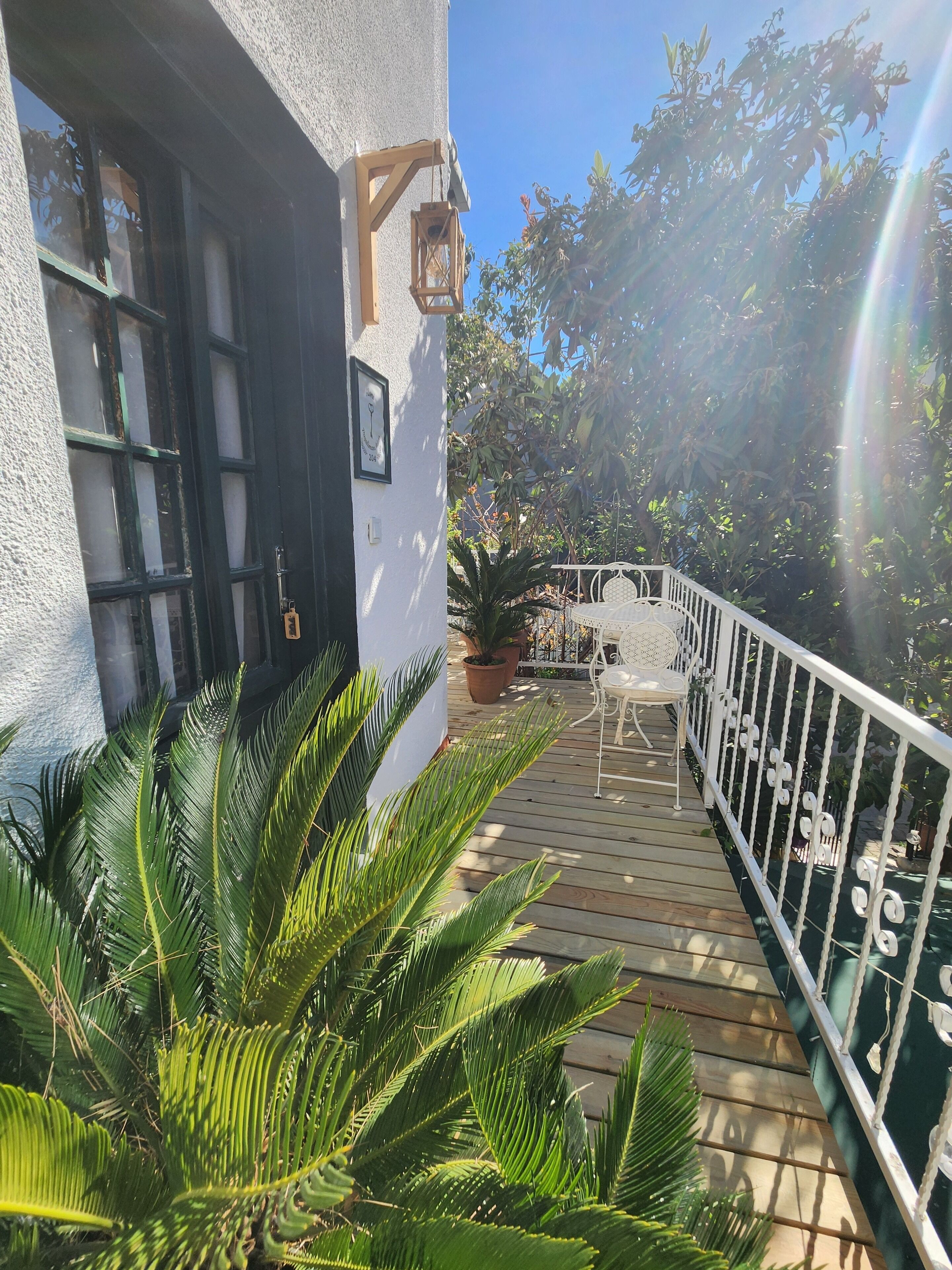Terraza de madera con sillas y barandilla blancos, rodeada de abundante vegetación.