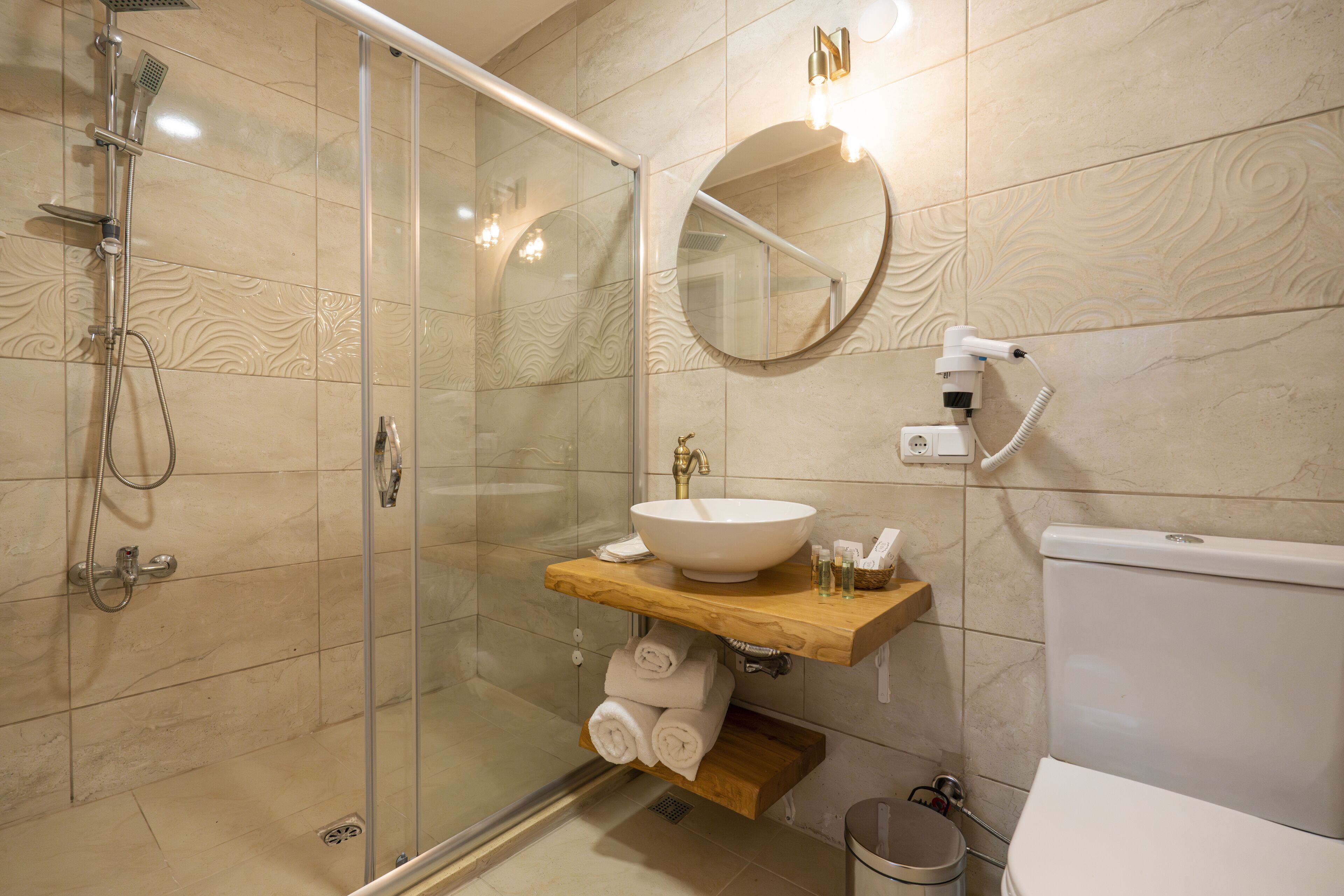 A modern bathroom with a glass shower enclosure, a round mirror, a wooden vanity with a sink, and a toilet.