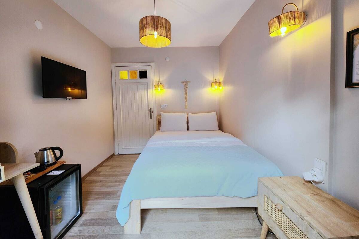 A bedroom with a bed, a television, a small refrigerator, and two wall-mounted lights.