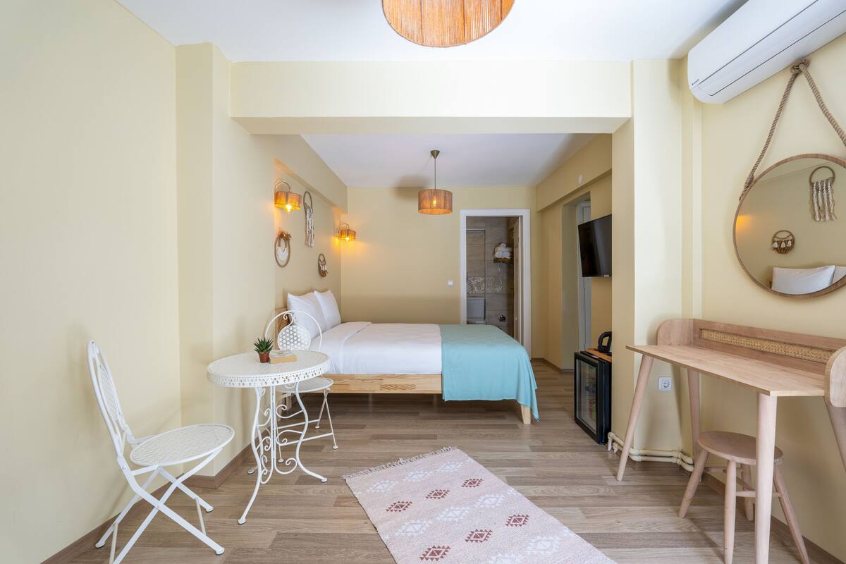A compact bedroom with a bed, a small desk, a chair, and a round mirror.