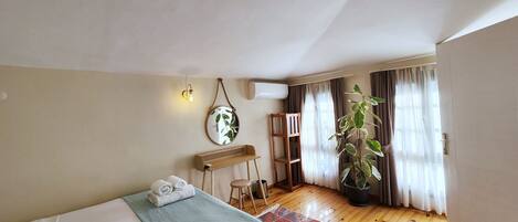 Un dormitorio con cama, una mesita, una silla, una planta en maceta y una ventana con cortinas.