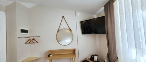 A small room with a TV, a mirror, a stool, a wooden table, and a shelf.
