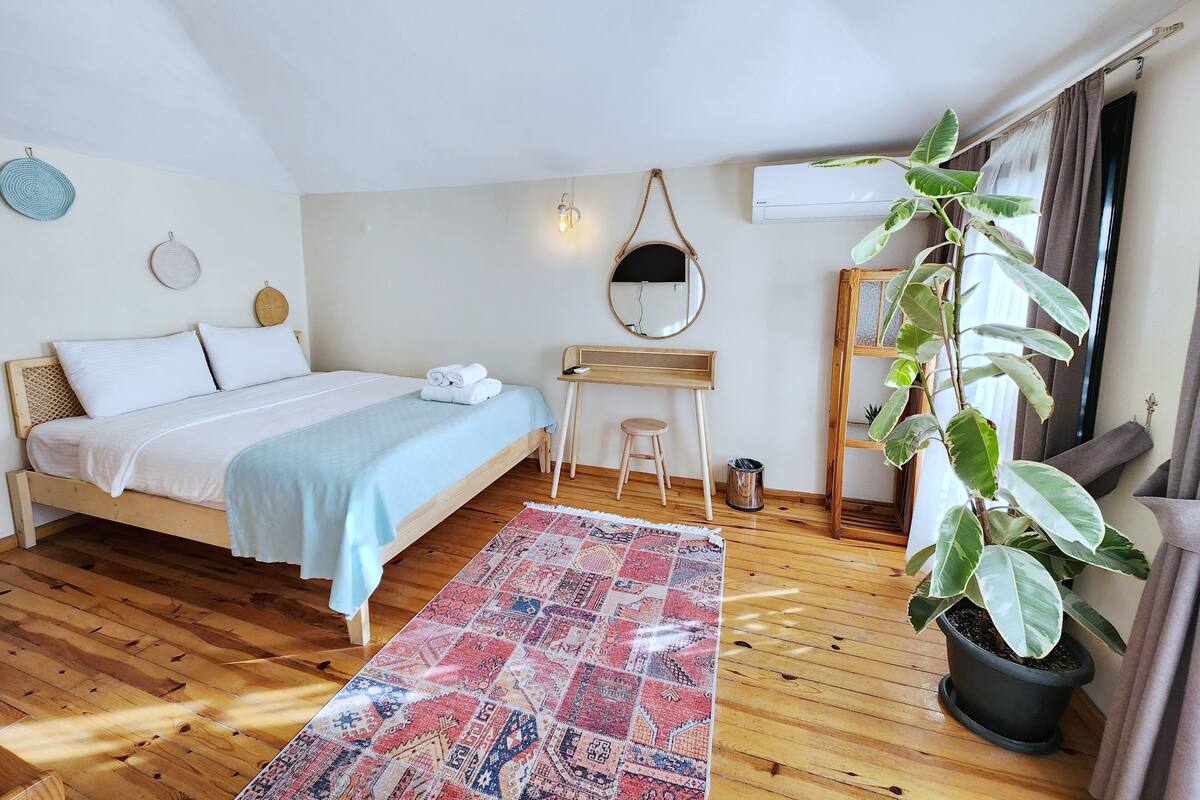 A bedroom with a bed, a desk, a chair, a potted plant, a rug, and a window with curtains.