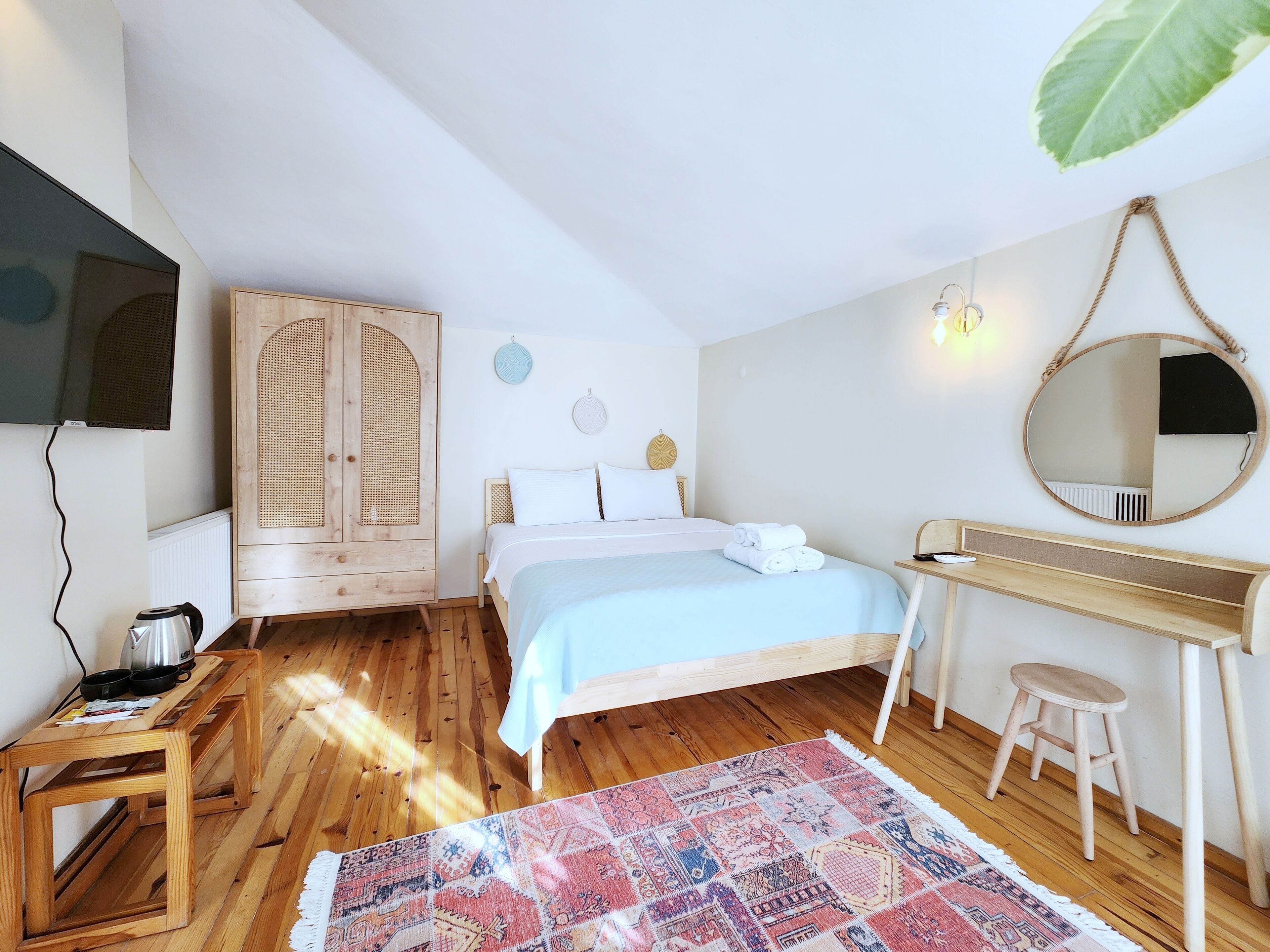A bedroom with a bed, wooden wardrobe, desk, and a mirror.