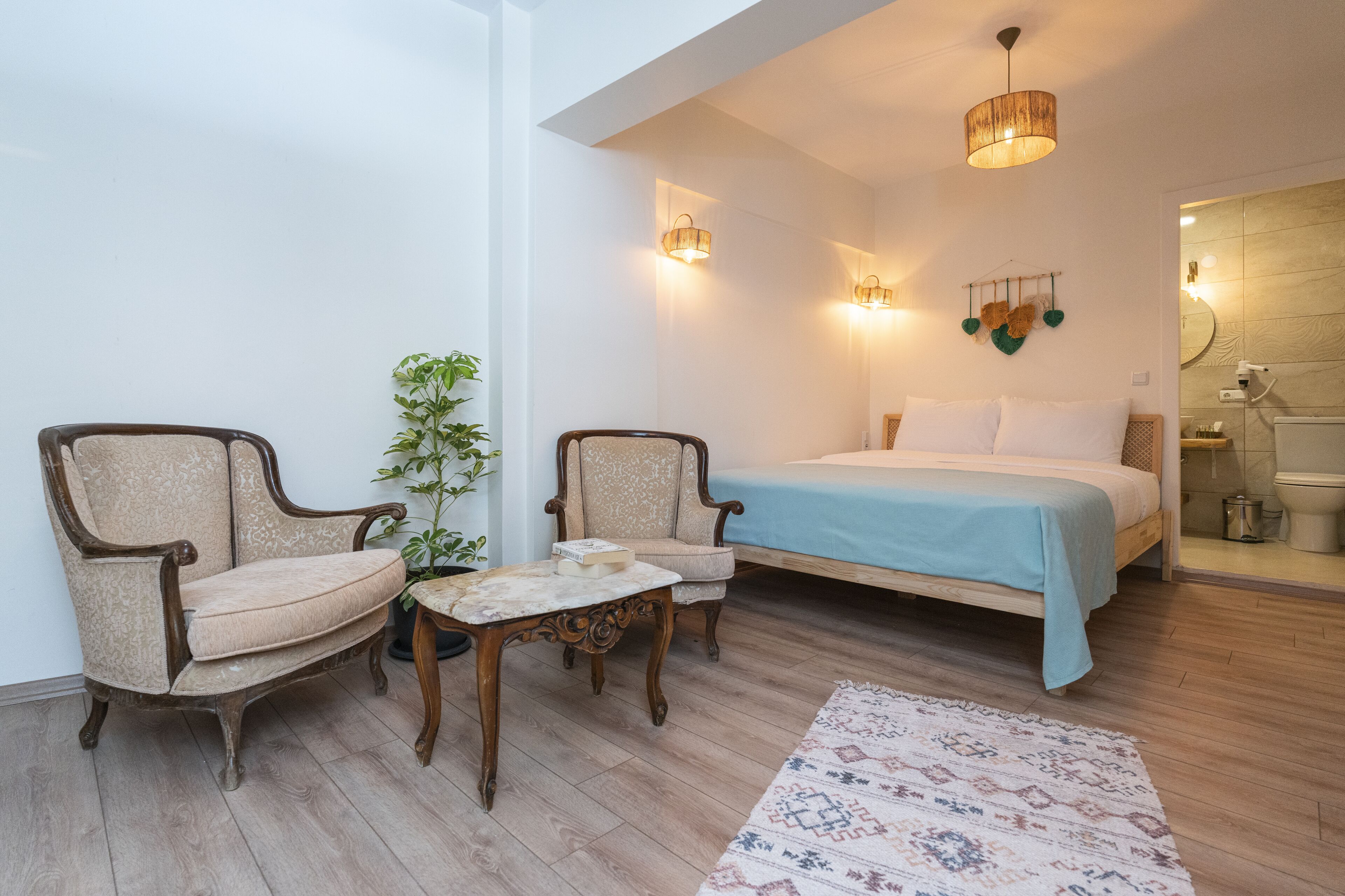 A bedroom with a bed, two armchairs, a small table, and a potted plant.