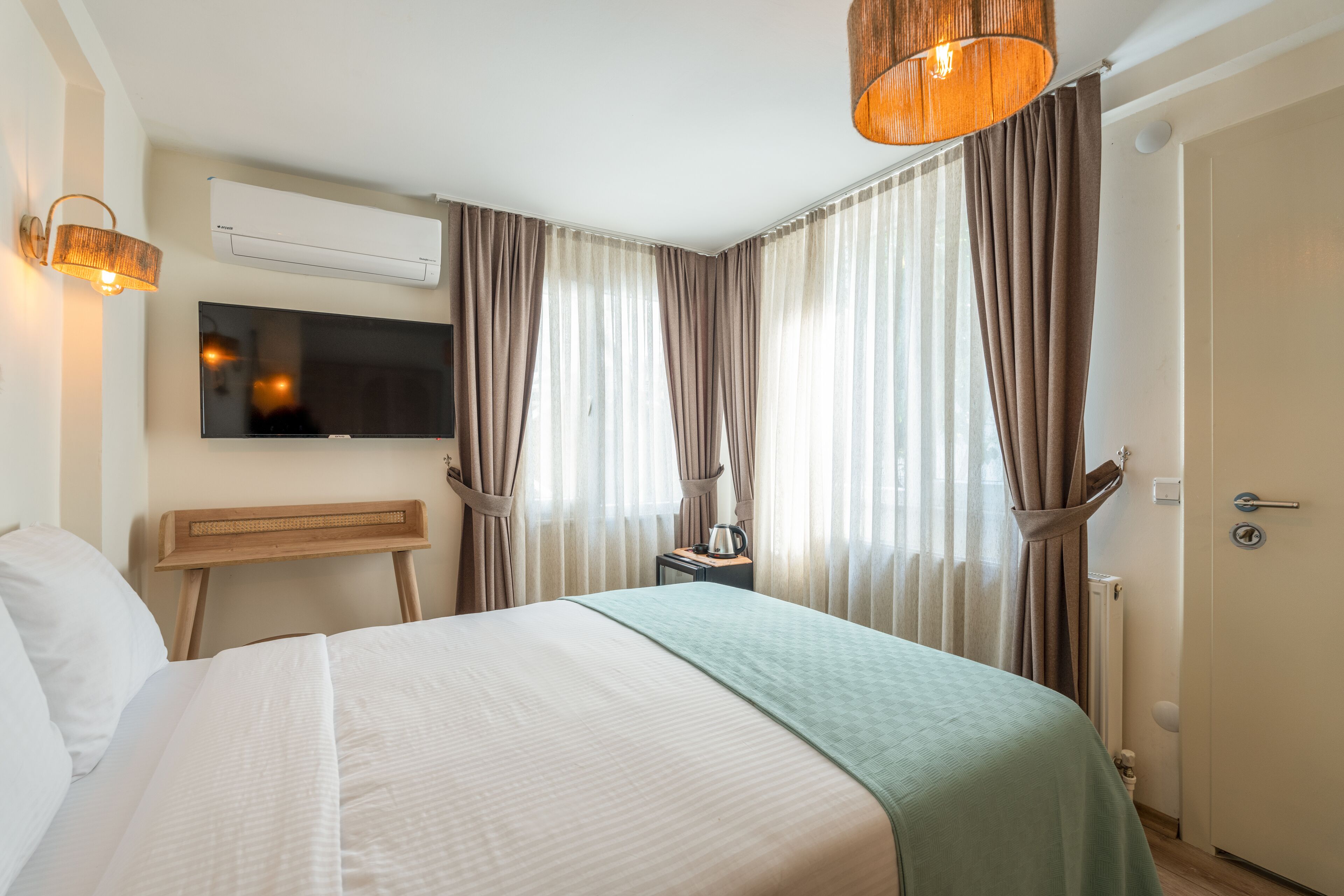A hotel room with a bed, a television, a bedside table with a kettle, and curtains.