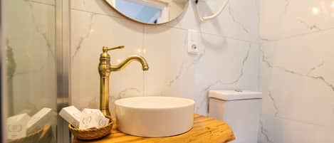 A bathroom with a marble wall, a white sink with a gold faucet, a wooden vanity, and a toilet.