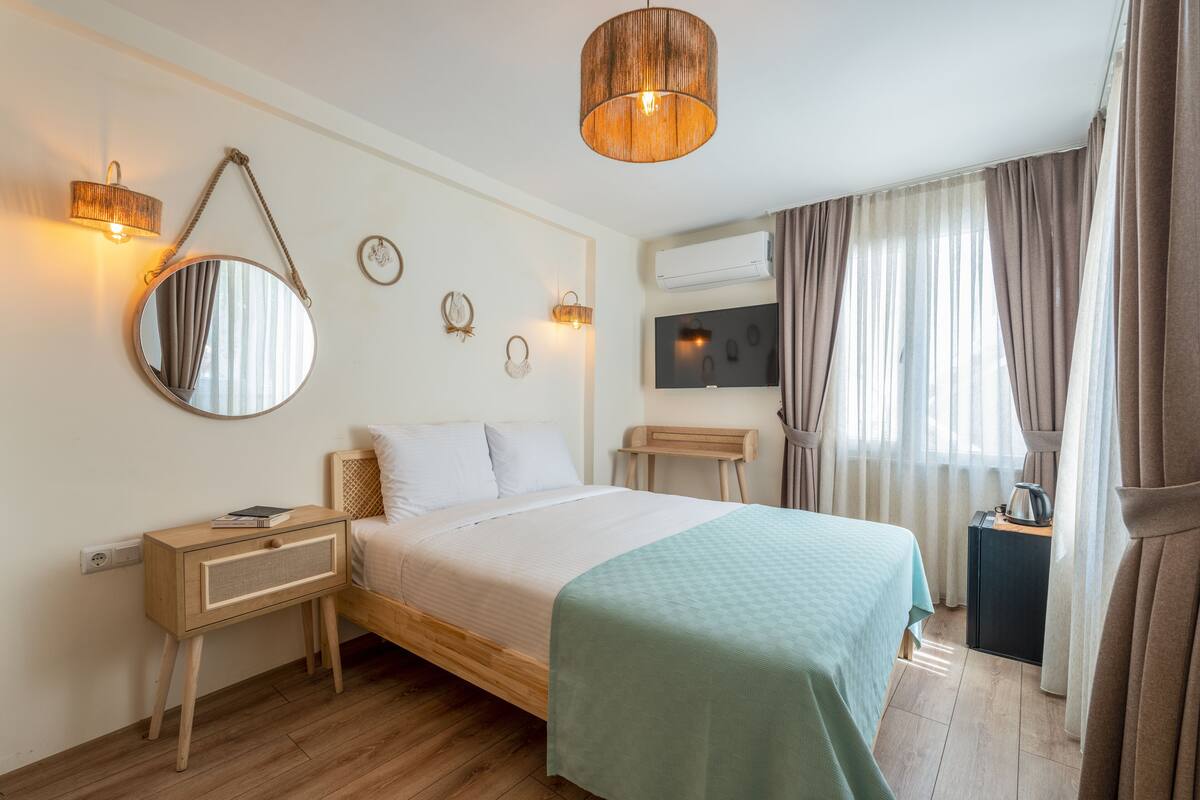 A neatly arranged bedroom with a bed, bedside table, mirror, wall-mounted lights, and an air conditioning unit.