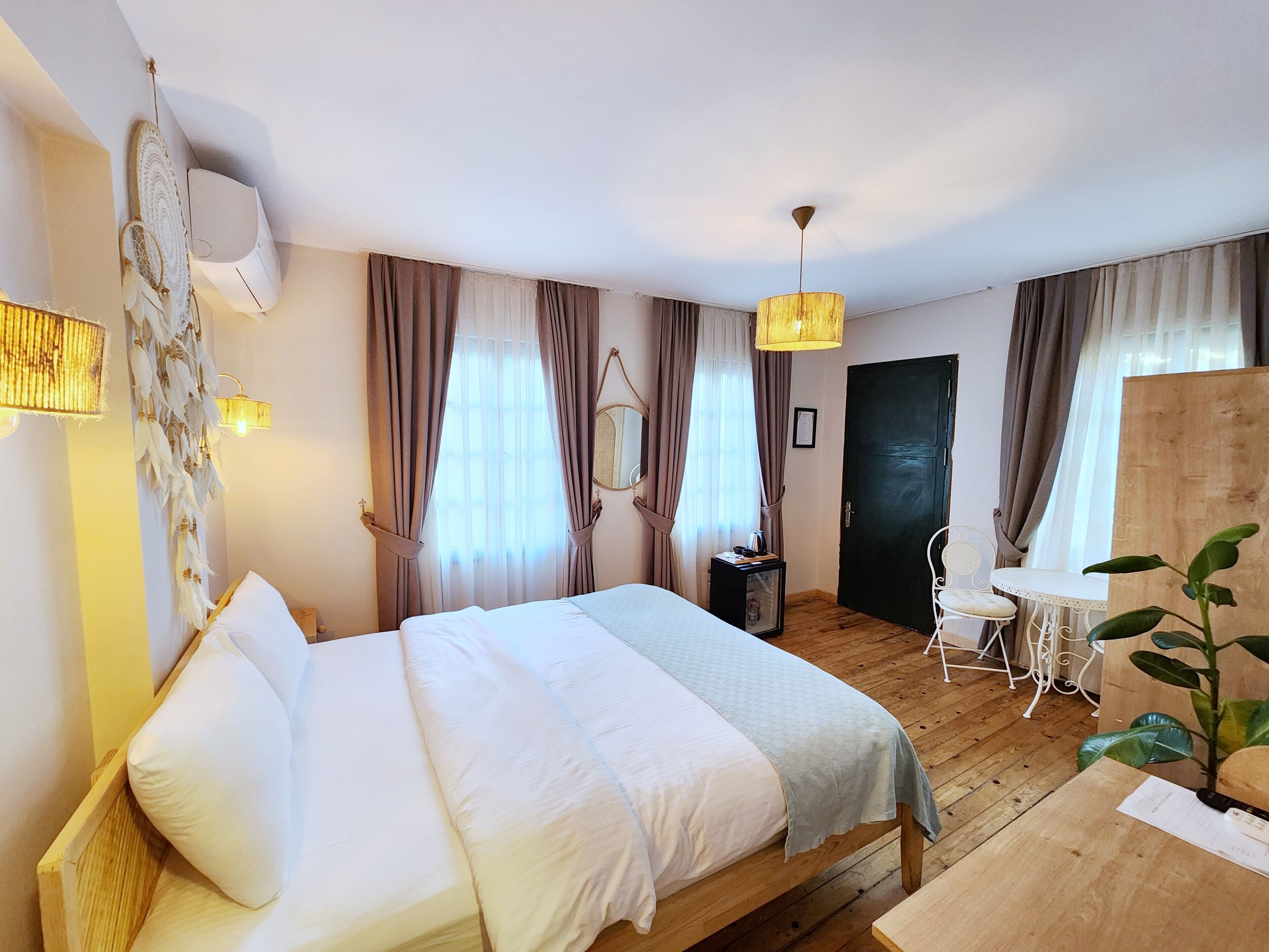 Een hotelkamer met een houten bed, een tafeltje, een stoel, een bureau en een potplant.