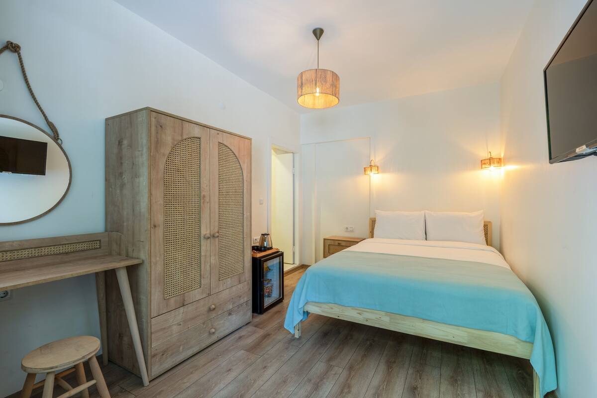 A bedroom with a bed, wooden wardrobe, desk, stool, and a wall-mounted mirror.