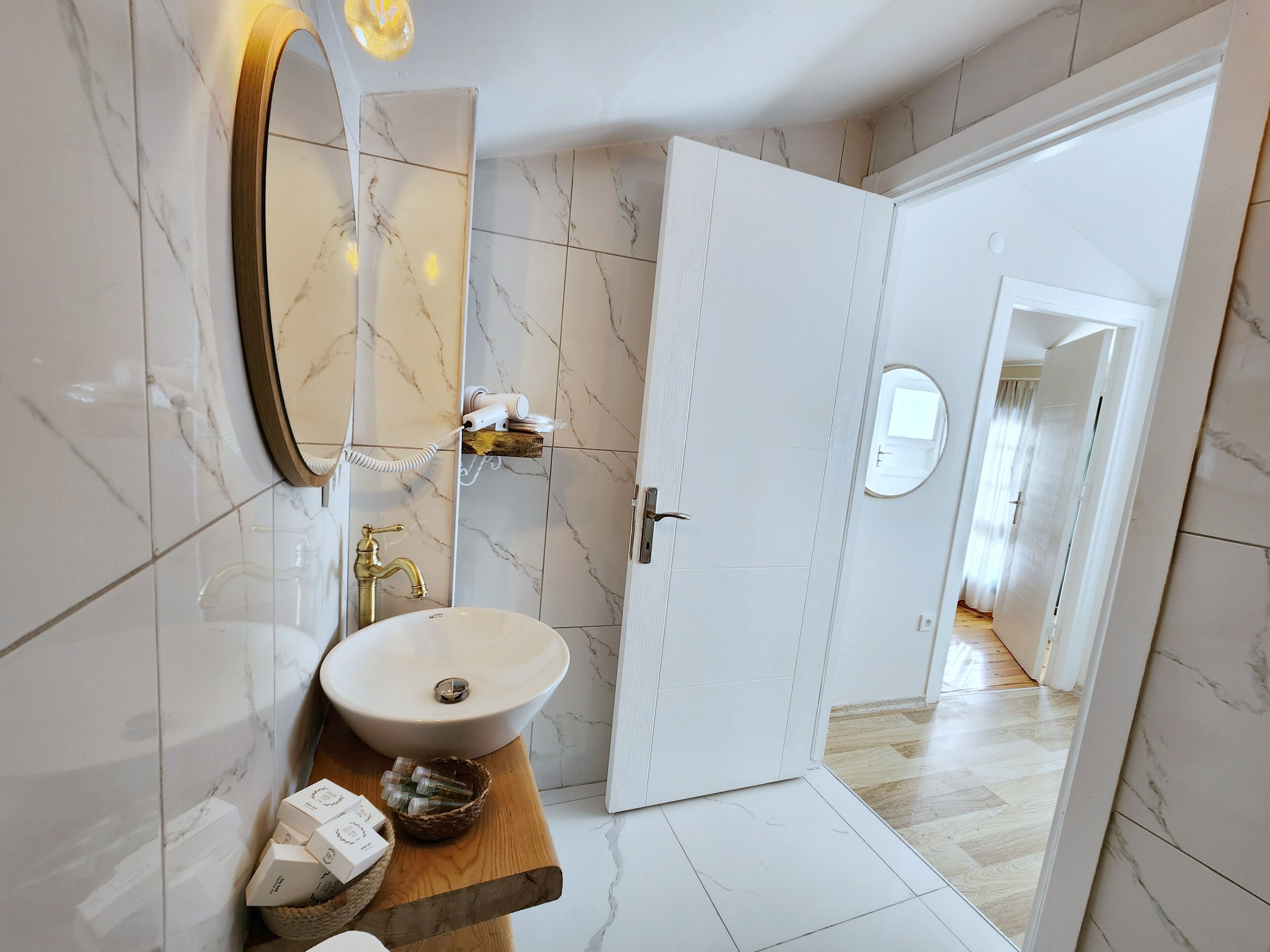 A modern bathroom with a marble backsplash, a white sink, a wooden vanity, and a door leading to another room.