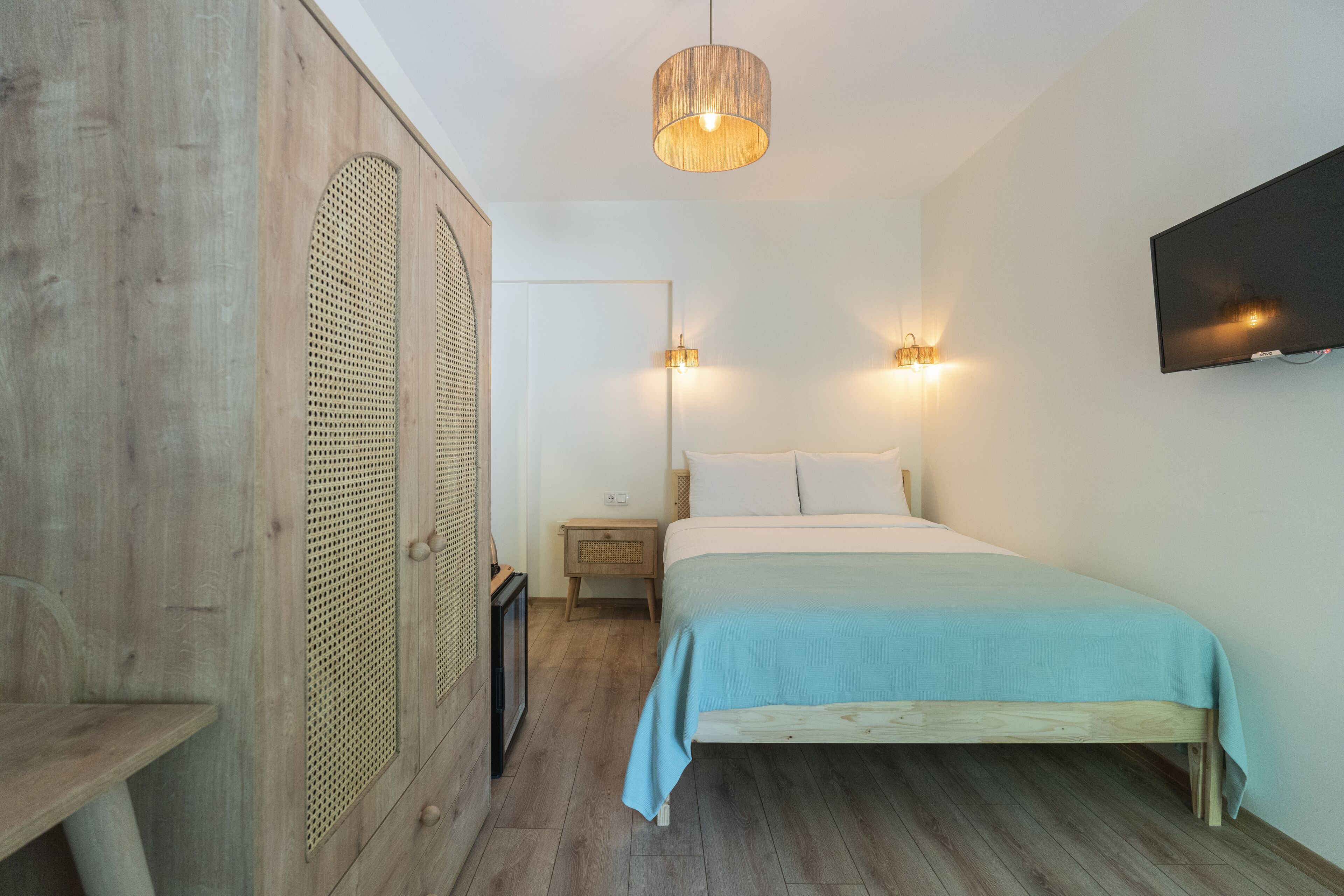 A bedroom with a wooden bed, a nightstand, a wall-mounted TV, and a hanging light fixture.