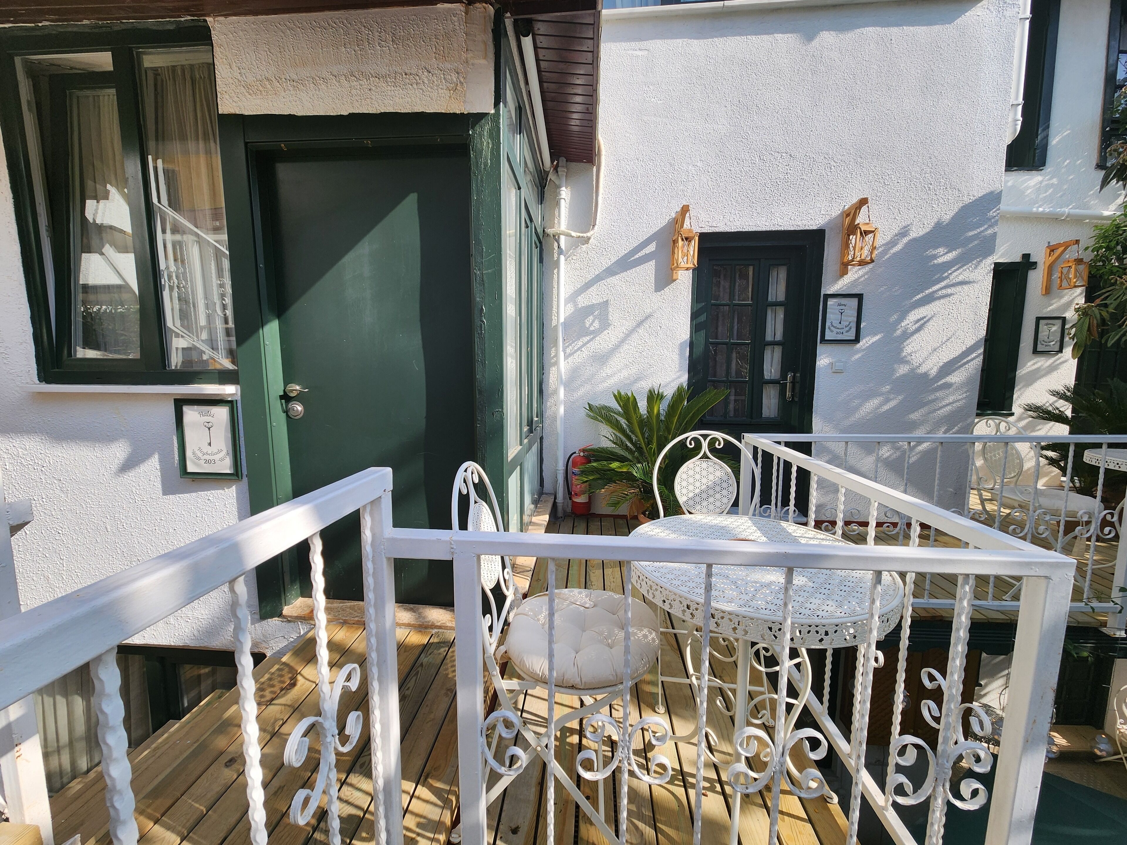 A wooden deck with a white metal railing, a green door, and a white wall with a window and a door.