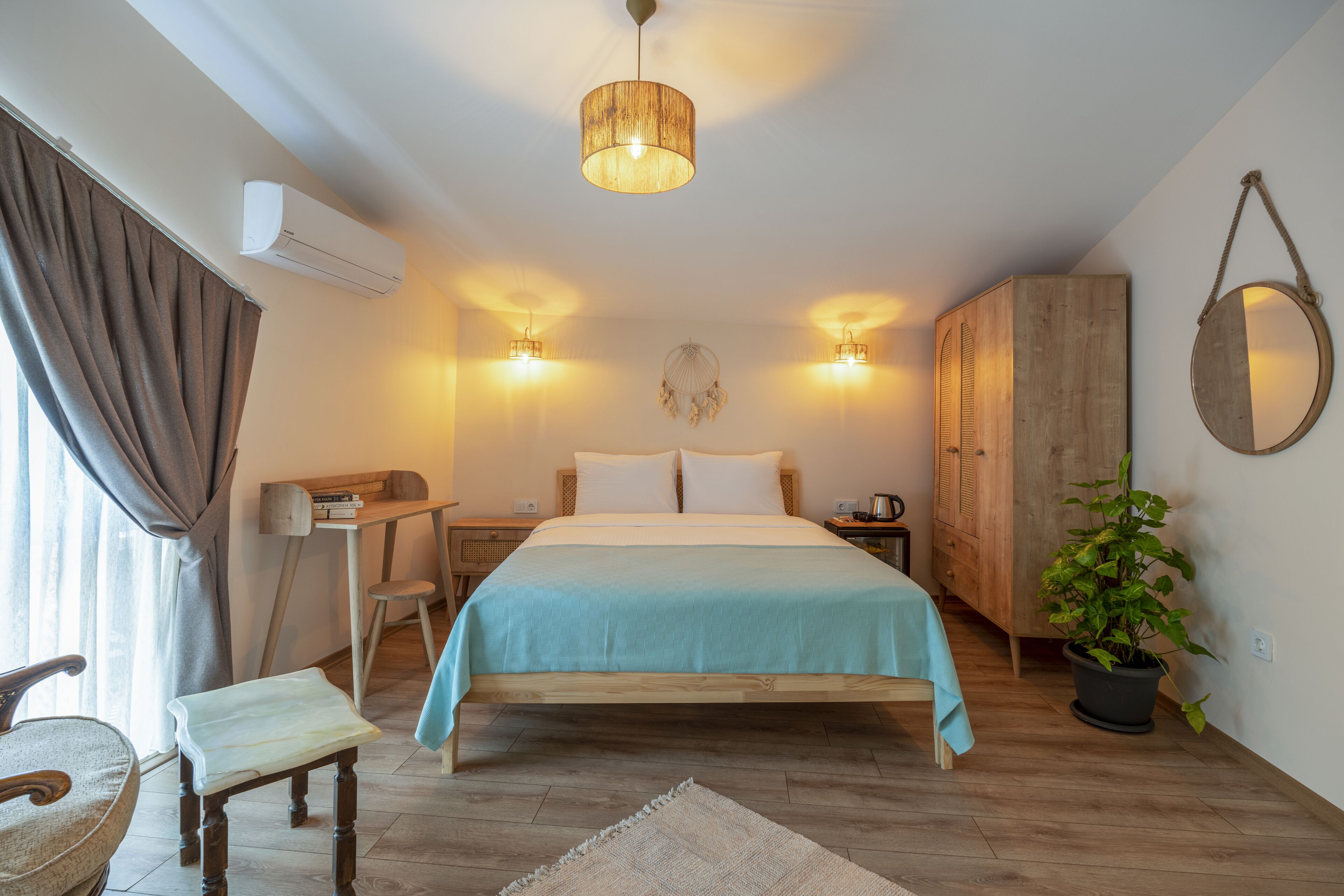 A bedroom with a bed, bedside tables, a desk, a chair, a potted plant, and a hanging light fixture.