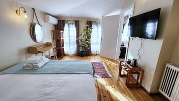 A hotel room with a large bed, a TV, a desk, a chair, a potted plant, and a window with curtains.