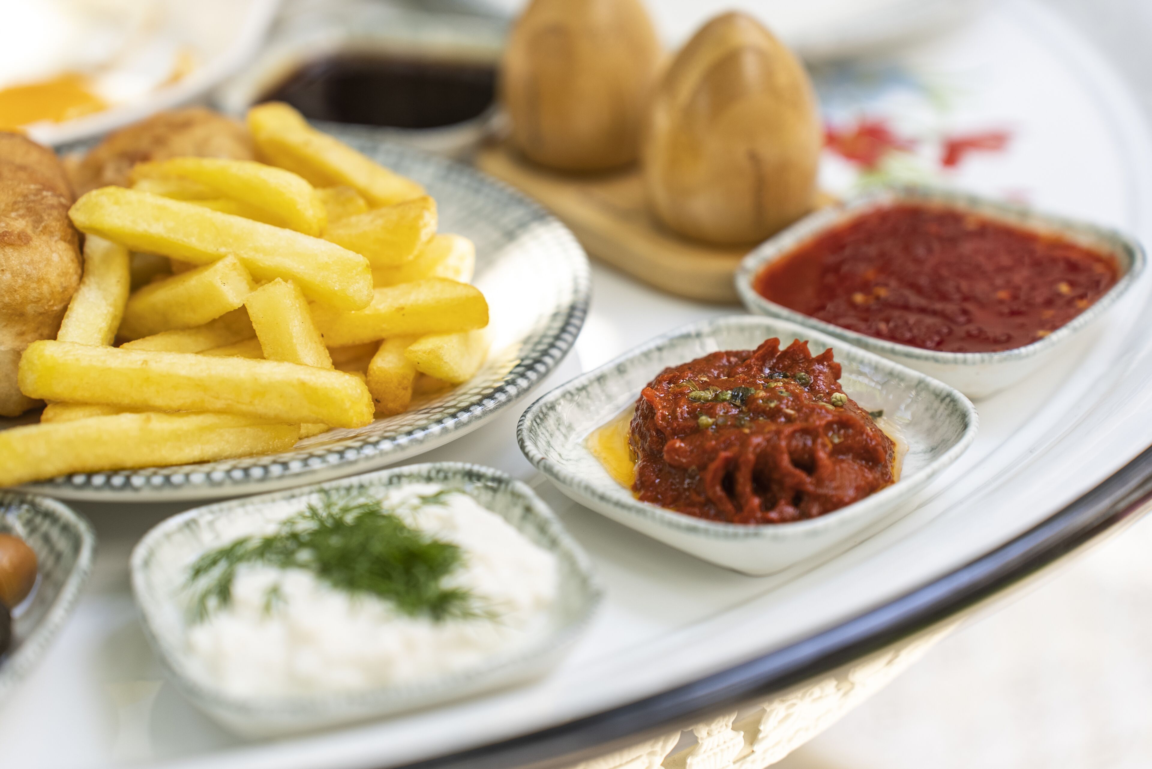A plate with French fries, a bread roll, and two small bowls of sauce.