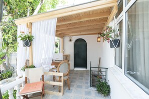 Zona d'estar a l'aire lliure acollidora amb una banca de fusta, una cadira i una taula. Hi ha testos penjants amb flors i una petita escala adossada a la paret.
