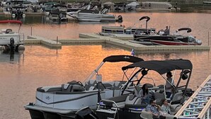 A marina with boats docked, a sunset in the background, and trees lining the shore.