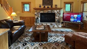A cozy living room with a stone fireplace, a leather sofa, a coffee table, and a flat-screen TV.