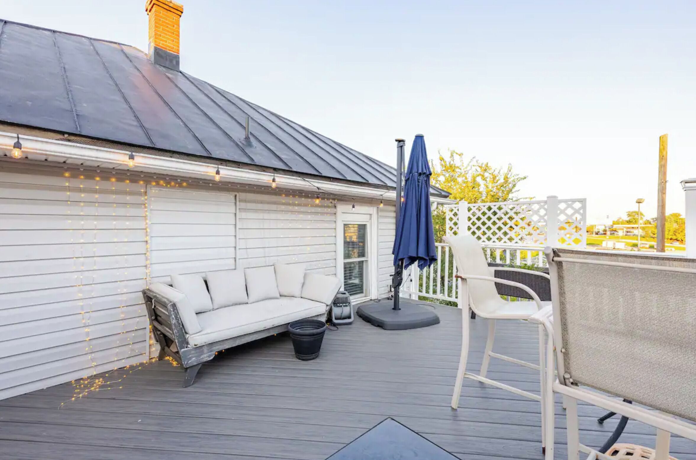 Una terraza techada con un sofá blanco, una sombrilla azul y una silla blanca.