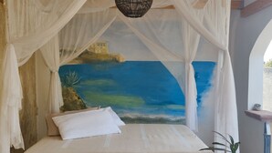 A bedroom with a bed, a canopy, a painting of a landscape, a wooden table with cups, and a vase with a flower.