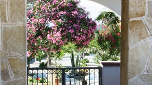 An arched stone doorway leading to a tiled patio area with a view of a pink flowering tree and a parked car.