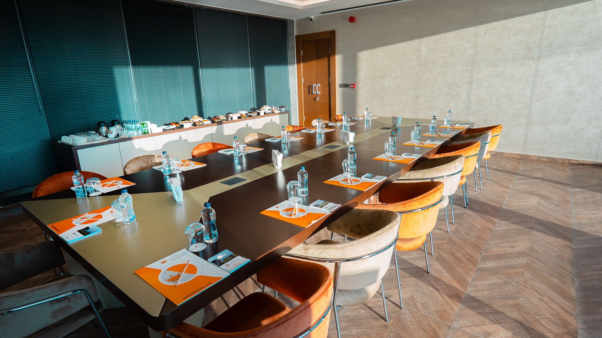 Uma sala de conferência com uma mesa comprida, cadeiras, garrafas de água e folhetos informativos.