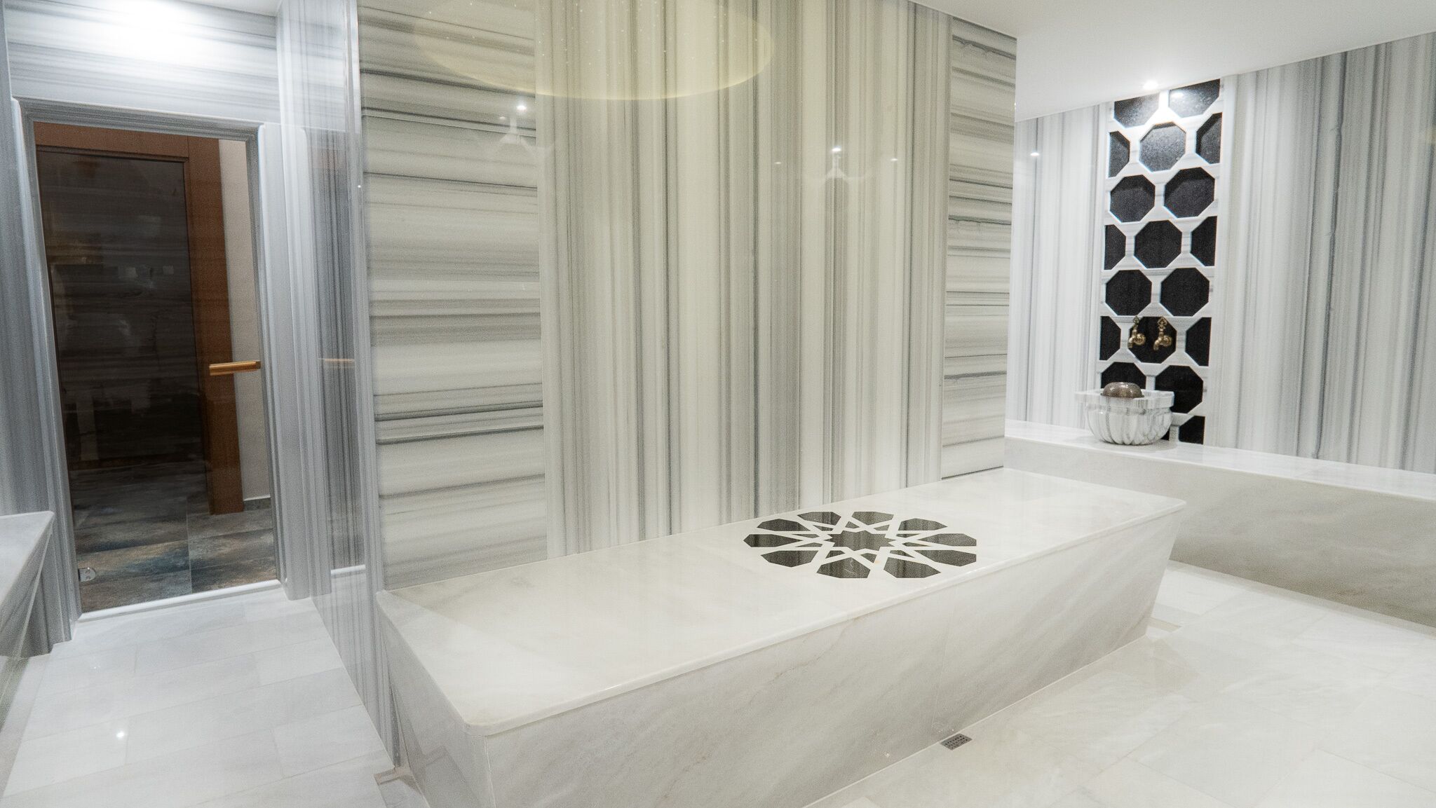 A modern bathroom with a large bathtub, a glass shower enclosure, and a decorative wall panel.