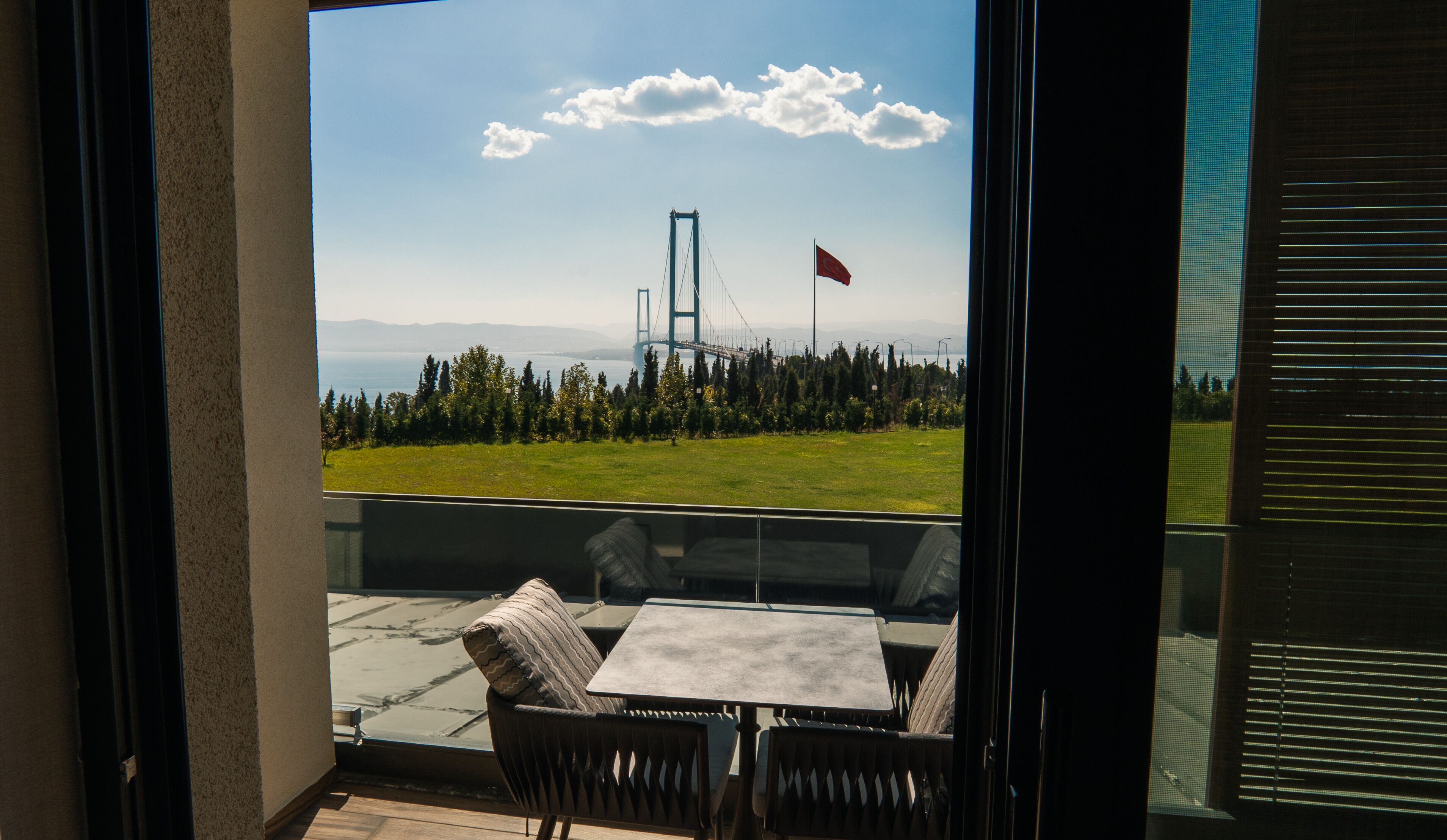 Un balcón con mesa y sillas, con vista a un puente y una bandera.