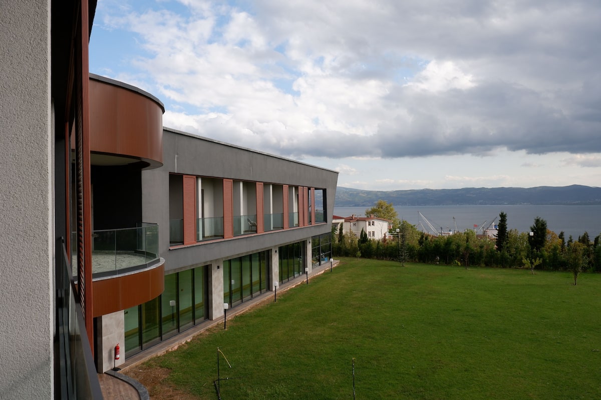A modern building with a curved balcony, large windows, and a view of a lake and mountains.