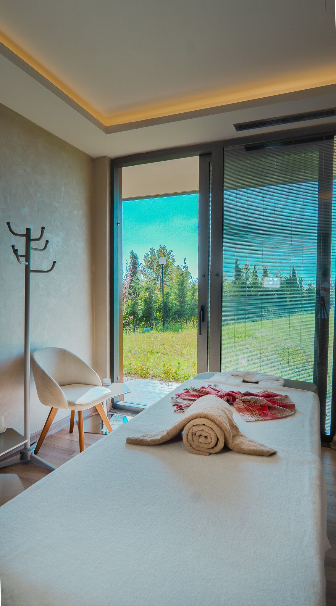 Quarto com uma cama grande, uma cadeira e vista para uma paisagem verde através de uma porta de vidro deslizante.