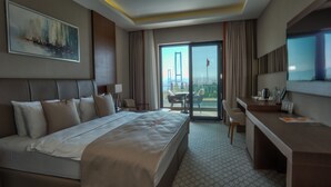 A hotel room with a large bed, a desk, a chair, a TV, and a balcony with a view of a bridge. - Motel Heksapolis (Dilovasi)
