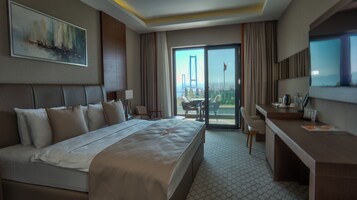 A hotel room with a large bed, a desk, a chair, a TV, and a balcony with a view of a bridge.