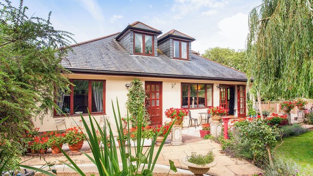 A house with a sloped roof, a front porch, and a garden with potted plants and flowers.