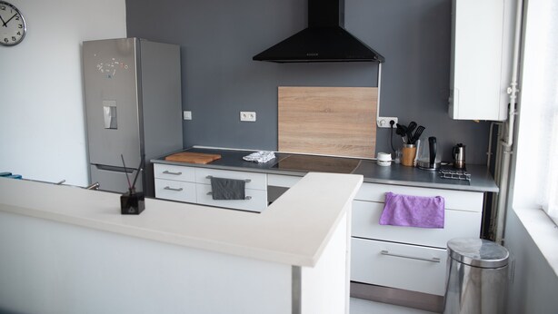 Une cuisine moderne dotée d’un réfrigérateur en acier inoxydable, d’un plan de travail en bois, d’une hotte noire et de meubles blancs.
