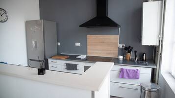 Une cuisine moderne dotée d’un réfrigérateur en acier inoxydable, d’un plan de travail en bois, d’une hotte noire et de meubles blancs.