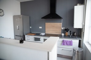 Eine moderne Küche mit einem Edelstahlkühlschrank, einer Holzarbeitsplatte, einer schwarzen Dunstabzugshaube und einem weißen Schrank.