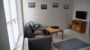 Un salon moderne comprenant un canapé, une table basse, un téléviseur et un meuble. Quatre tableaux encadrés sont accrochés au mur.