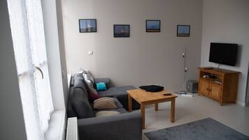 Un salon moderne comprenant un canapé, une table basse, un téléviseur et un meuble. Quatre tableaux encadrés sont accrochés au mur.
