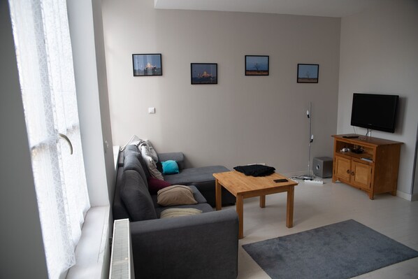 Ein modernes Wohnzimmer mit einer Couch, einem Couchtisch, einem Fernseher und einem Schrank. An der Wand hängen vier gerahmte Bilder.