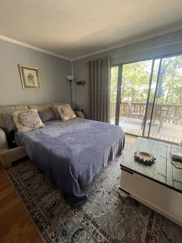 Een slaapkamer met een bed, nachtkastje, stoel, raam met gordijnen en uitzicht op de omgeving.