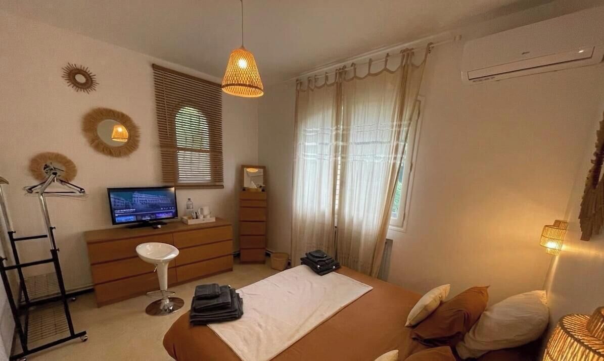 Quarto com uma cama, escrivaninha, cadeira, televisão e janela com cortinas.
